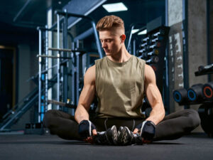 Man doing butterfly stretch on floor in gym.