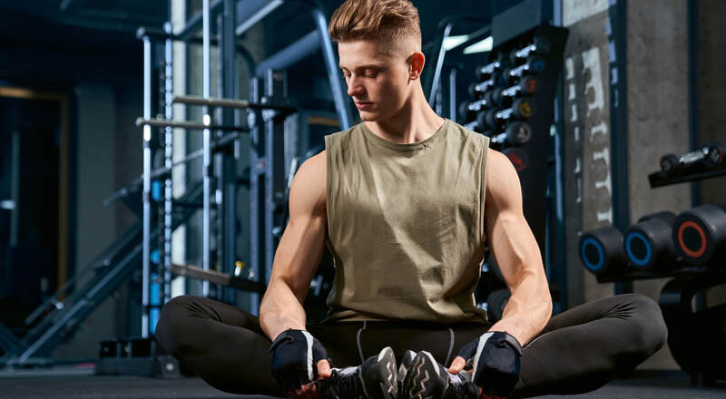 Man doing butterfly stretch on floor in gym.